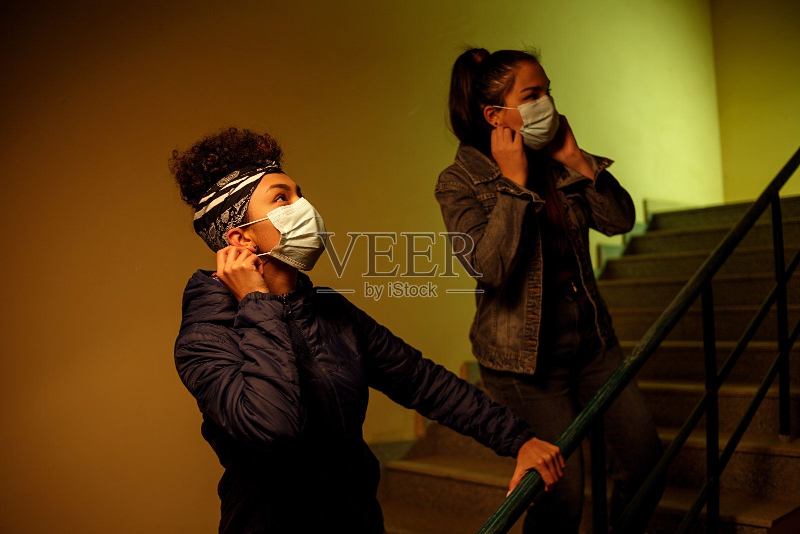 佩戴医用口罩的亚非女孩在楼梯间躲避病毒感染者照片摄影图片