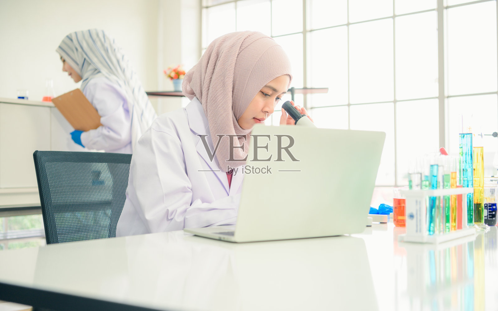 专注的穆斯林女科学家在化学实验室的实验中用显微镜观察照片摄影图片