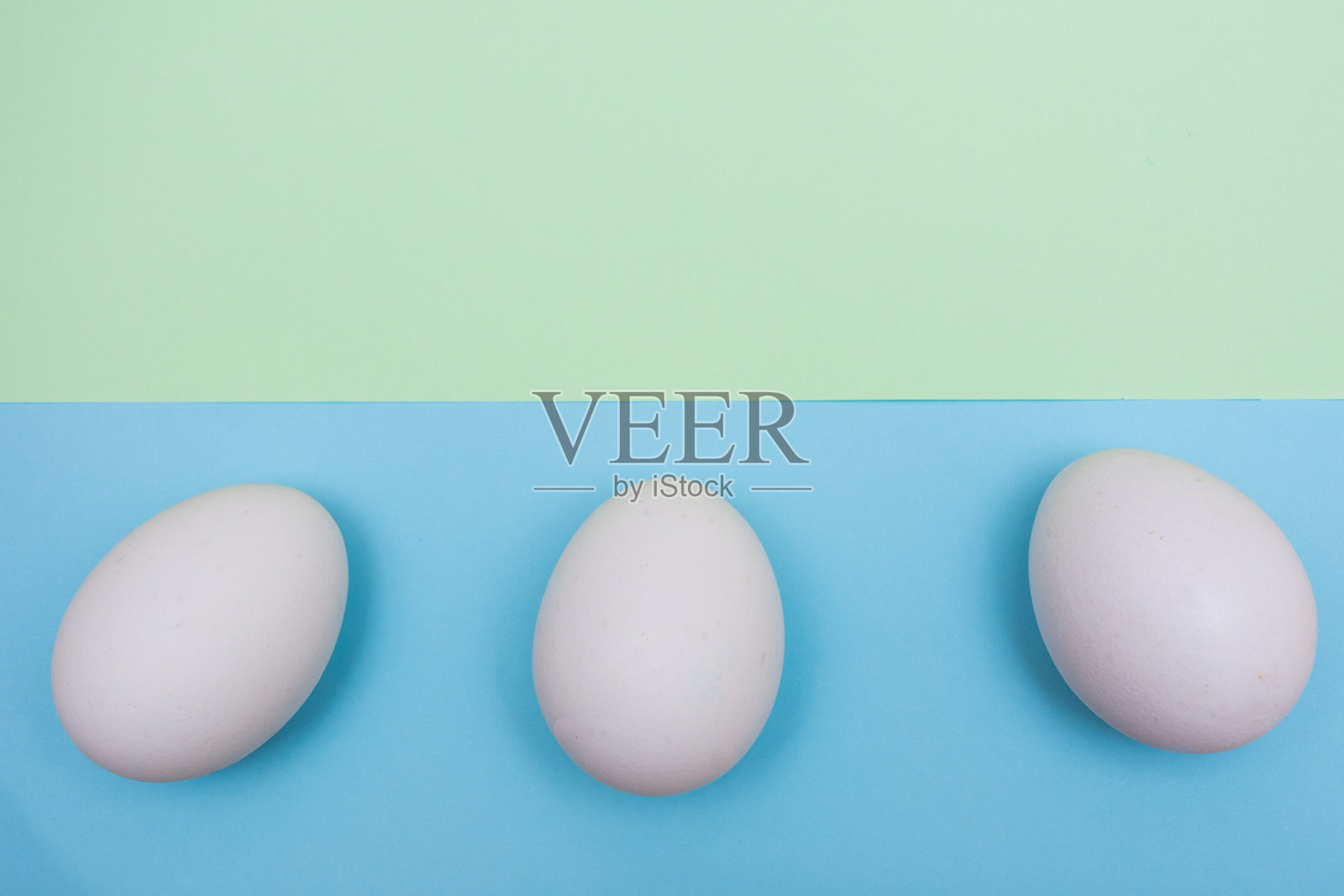 三个复活节假期平铺白色鸡蛋在坚实的浅绿色上，蓝色的粉彩背景，上面有复制空间。照片摄影图片