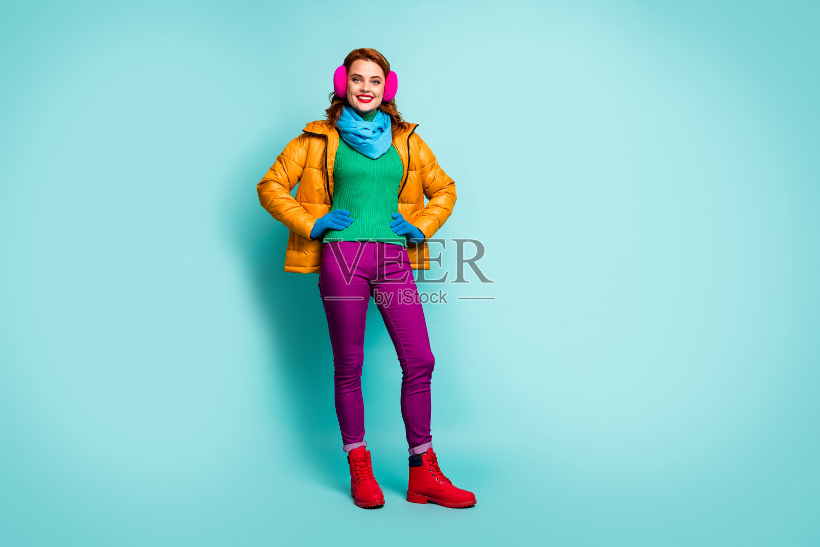 尽情享受秋冬假期的女人的长照片，把手放在腰穿休闲亮衣服孤立在绿松石色的背景照片摄影图片