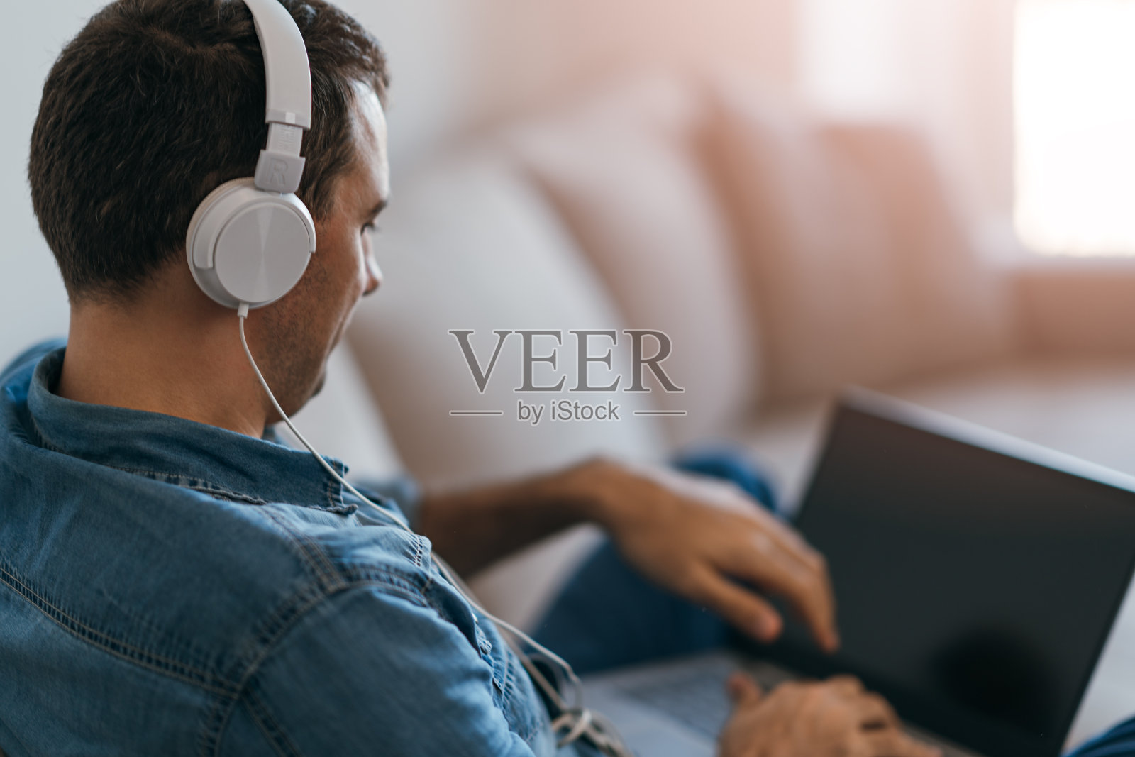 男人戴着耳机在沙发上使用笔记本电脑照片摄影图片