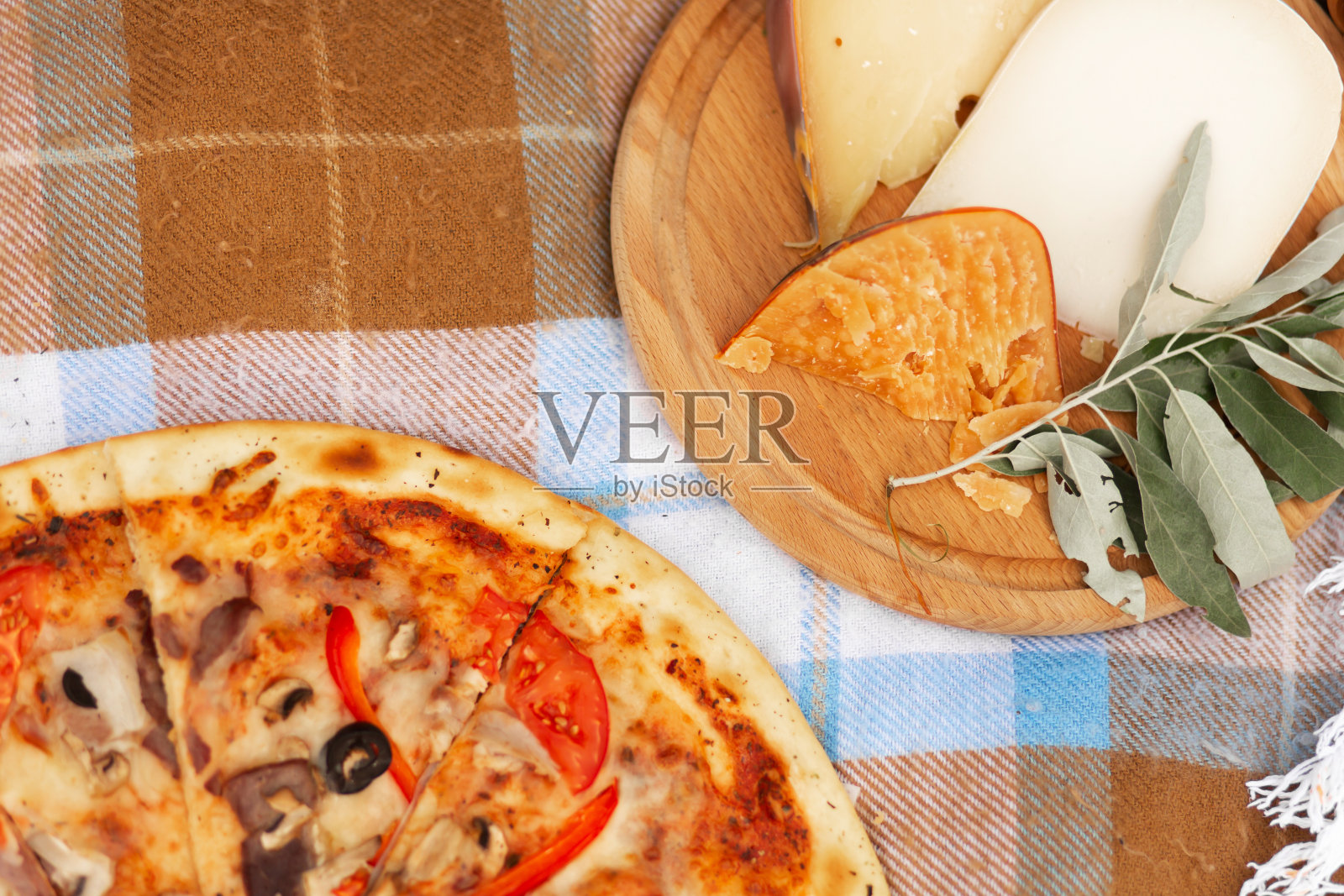 方格床单上放着披萨和奶酪拼盘。夏季野餐照片摄影图片