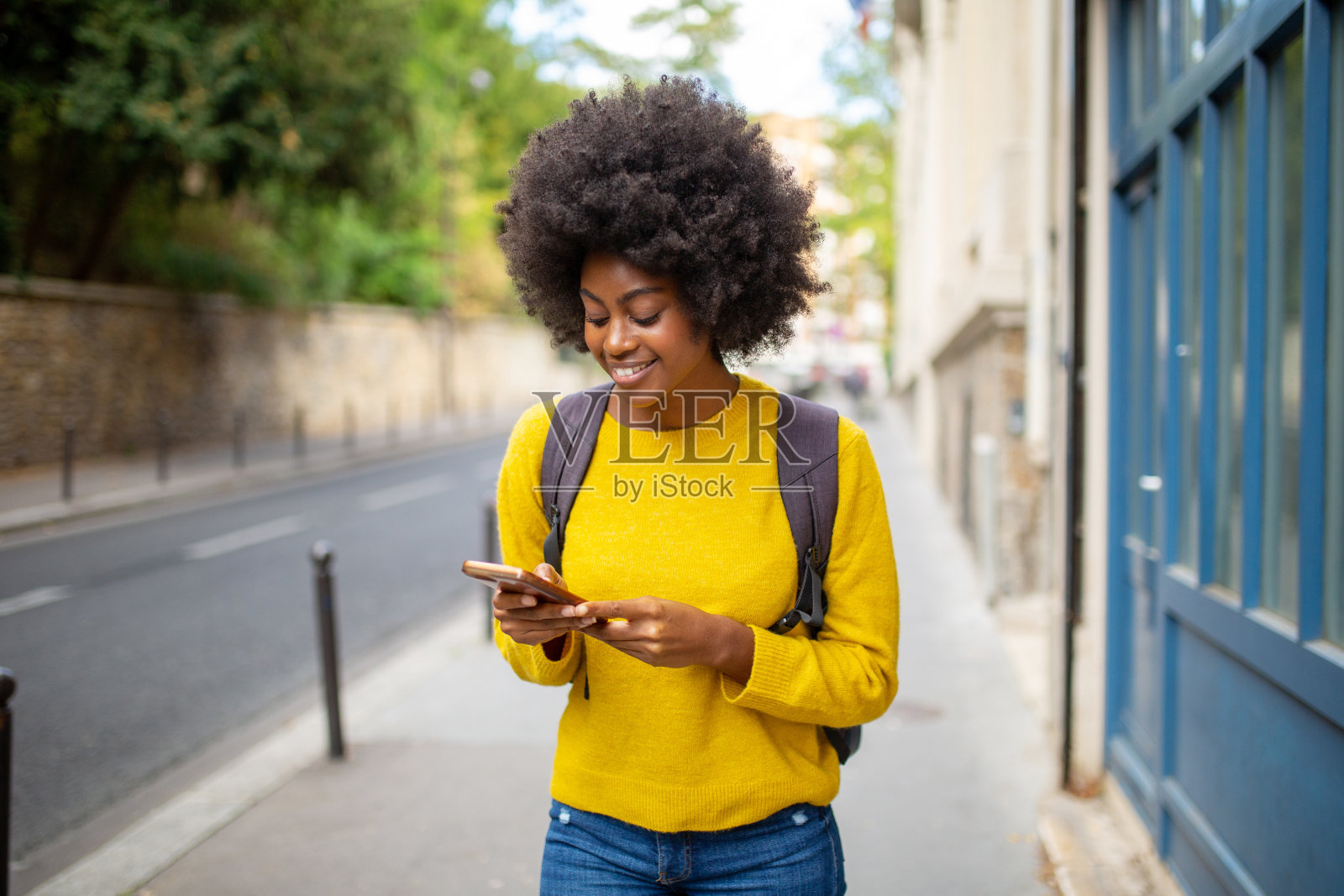 微笑的年轻非洲裔美国女性挎着手机和包包走在城市里照片摄影图片