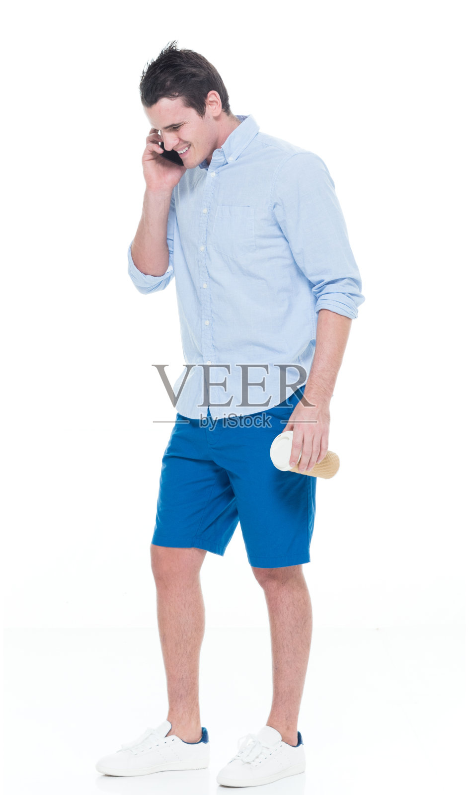 白人年轻男性穿着帆布鞋站在白色背景前，使用智能手机照片摄影图片