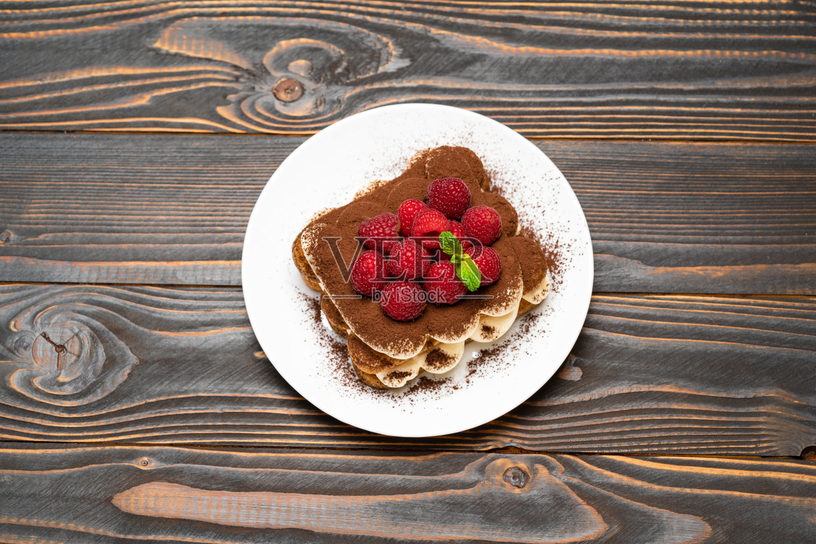 经典提拉米苏甜点，木背景的陶瓷盘子上有覆盆子照片摄影图片