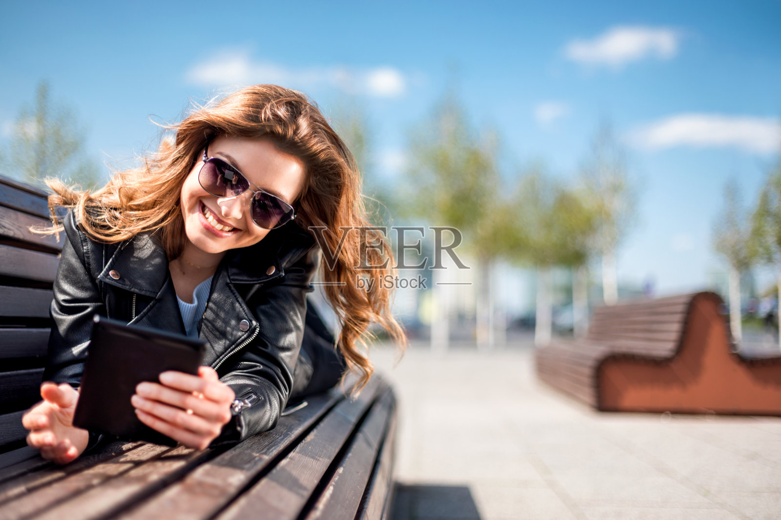 女性坐在城市空间的长椅上，在城市中使用平板电脑照片摄影图片