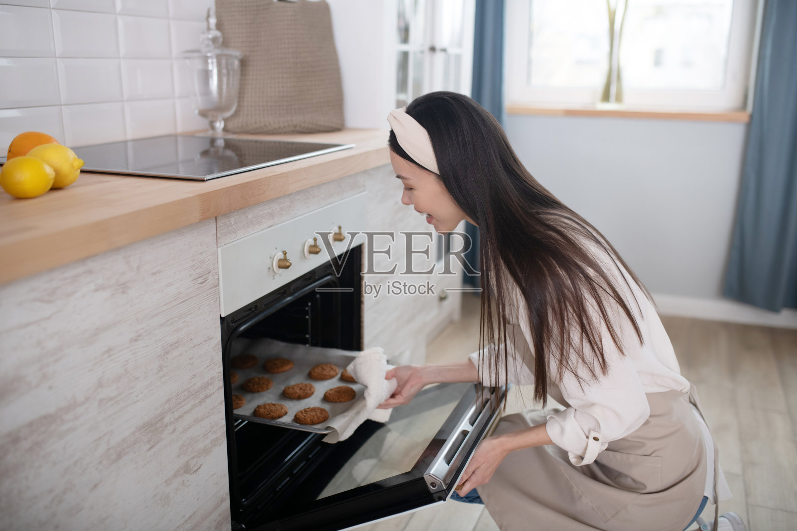 年轻女孩家庭主妇坐在烤箱旁取出烤盘照片摄影图片
