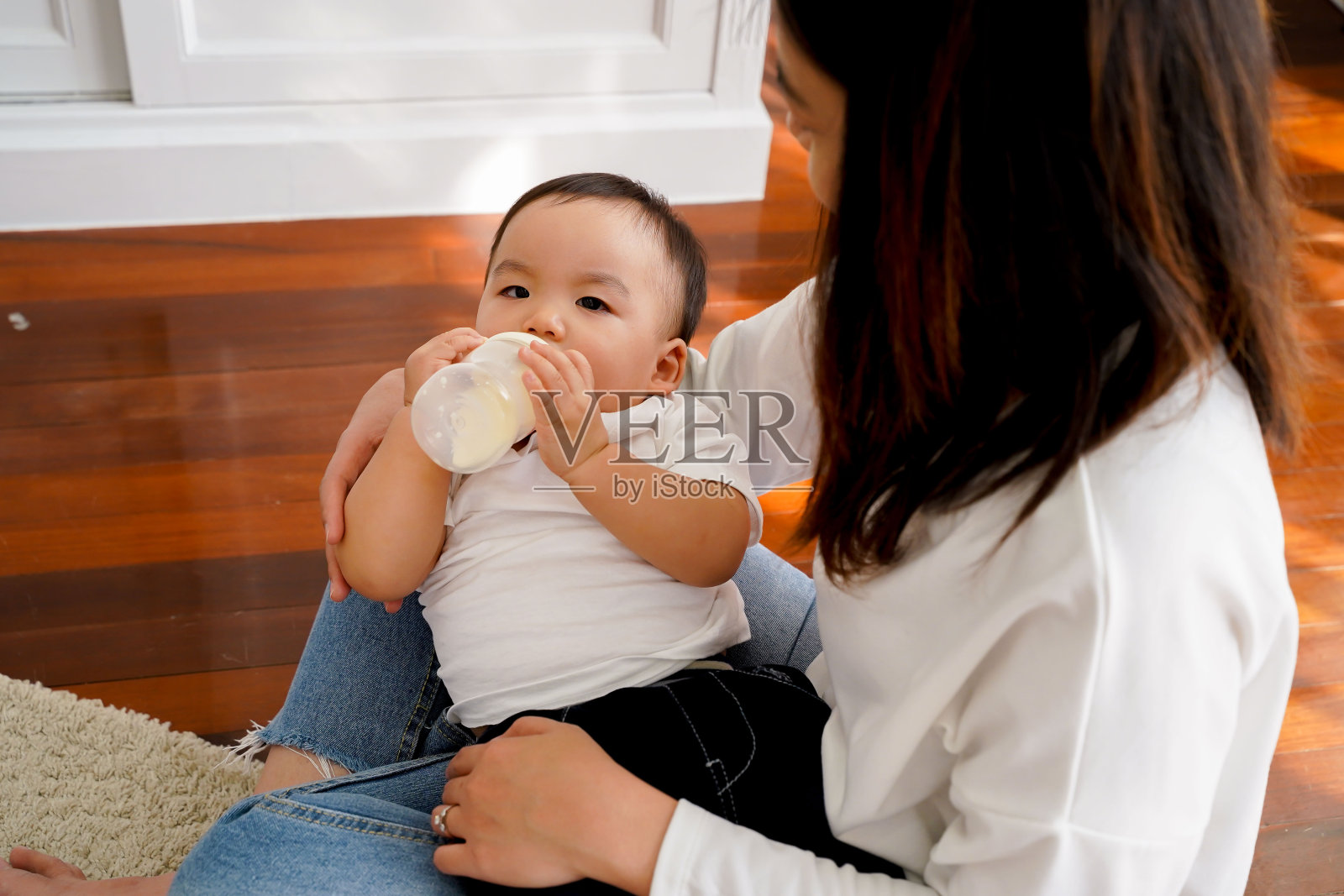 亚洲母亲特写：在客厅里照顾自己的儿子，用奶瓶喂奶——母性和配方奶喂养的新生儿概念照片摄影图片