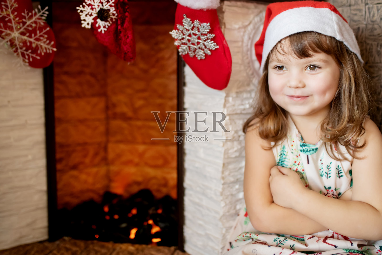 可爱的微笑小女孩戴着圣诞帽在美丽的客厅与传统的壁炉装饰圣诞节。照片摄影图片