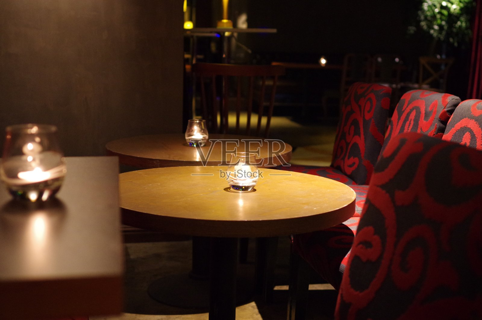 在空荡荡的休息室里，圆形木酒吧桌子上的玻璃烛台上燃烧着蜡烛照片摄影图片