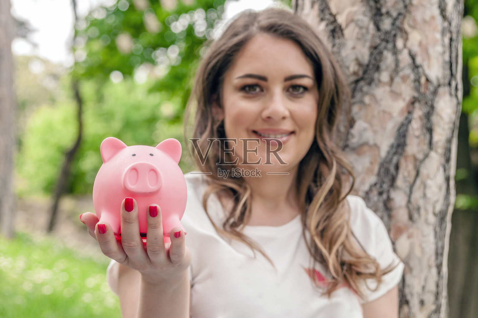 特写肖像快乐，微笑的商业女人，抱着储蓄罐，孤立的户外绿树背景。金融储蓄，银行概念。积极的情绪，面部表情照片摄影图片