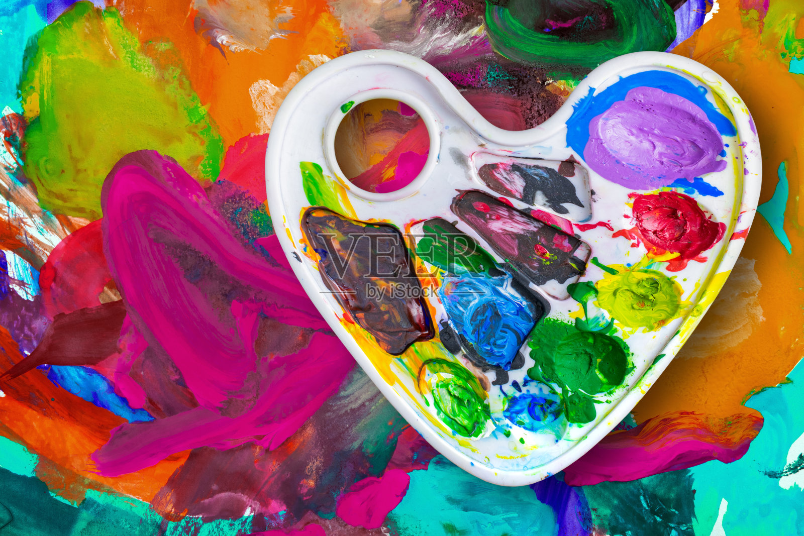 心形的艺术调色板，配上颜料，映衬着五彩缤纷的背景照片摄影图片