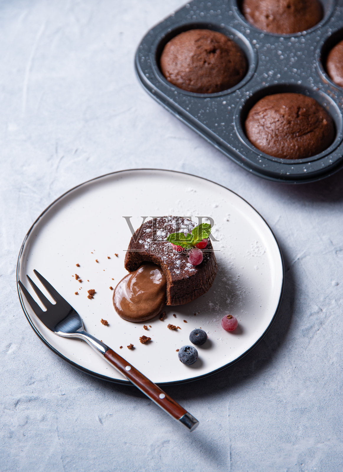 新鲜热的纯素巧克力软糖熔岩和浆果在一个白色的盘子在蓝灰色的背景照片摄影图片