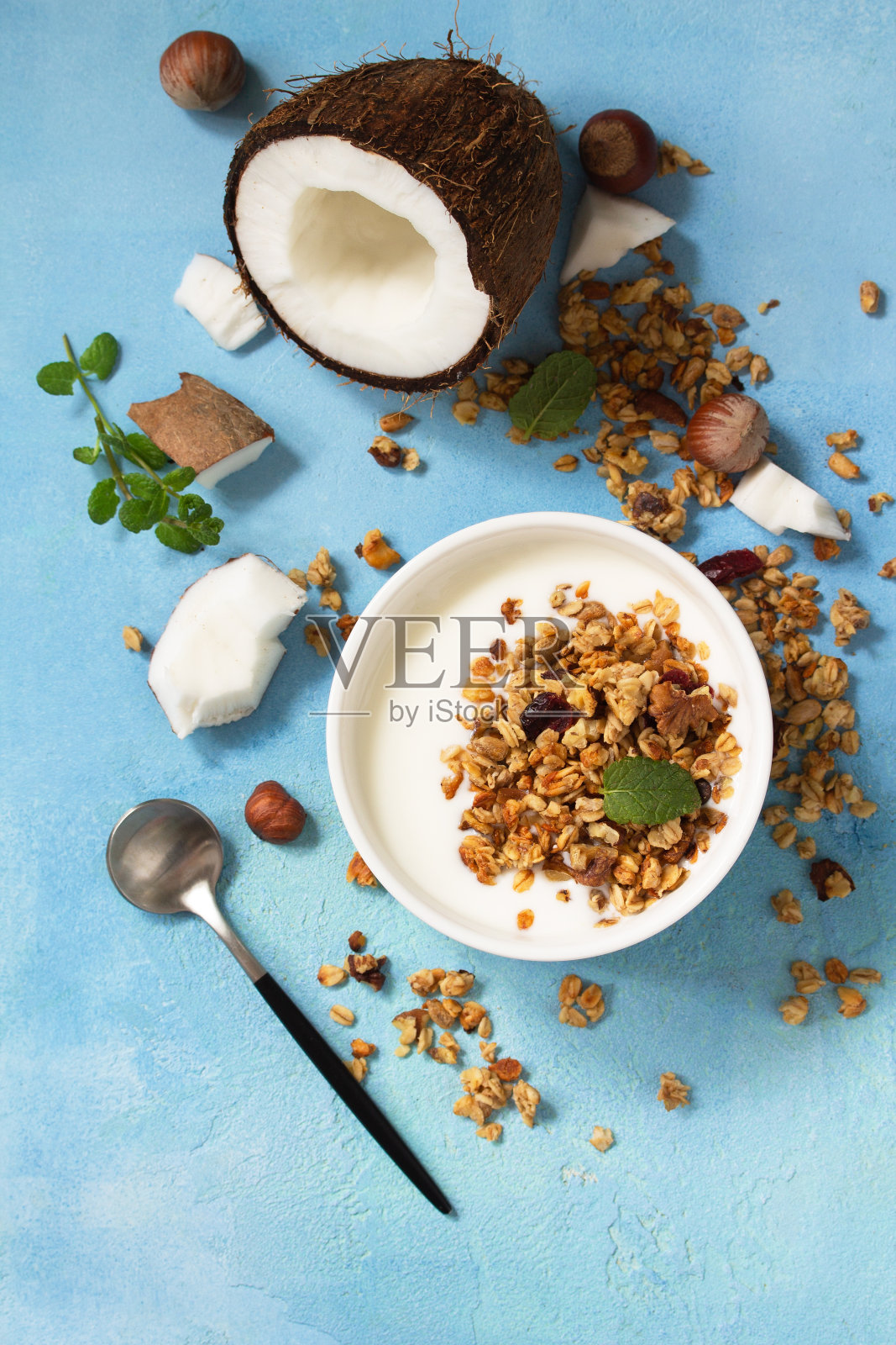 自制健康的早餐。一碗自制的烤椰子麦片和希腊酸奶放在绿松石或混凝土桌上。俯视图平铺背景。照片摄影图片