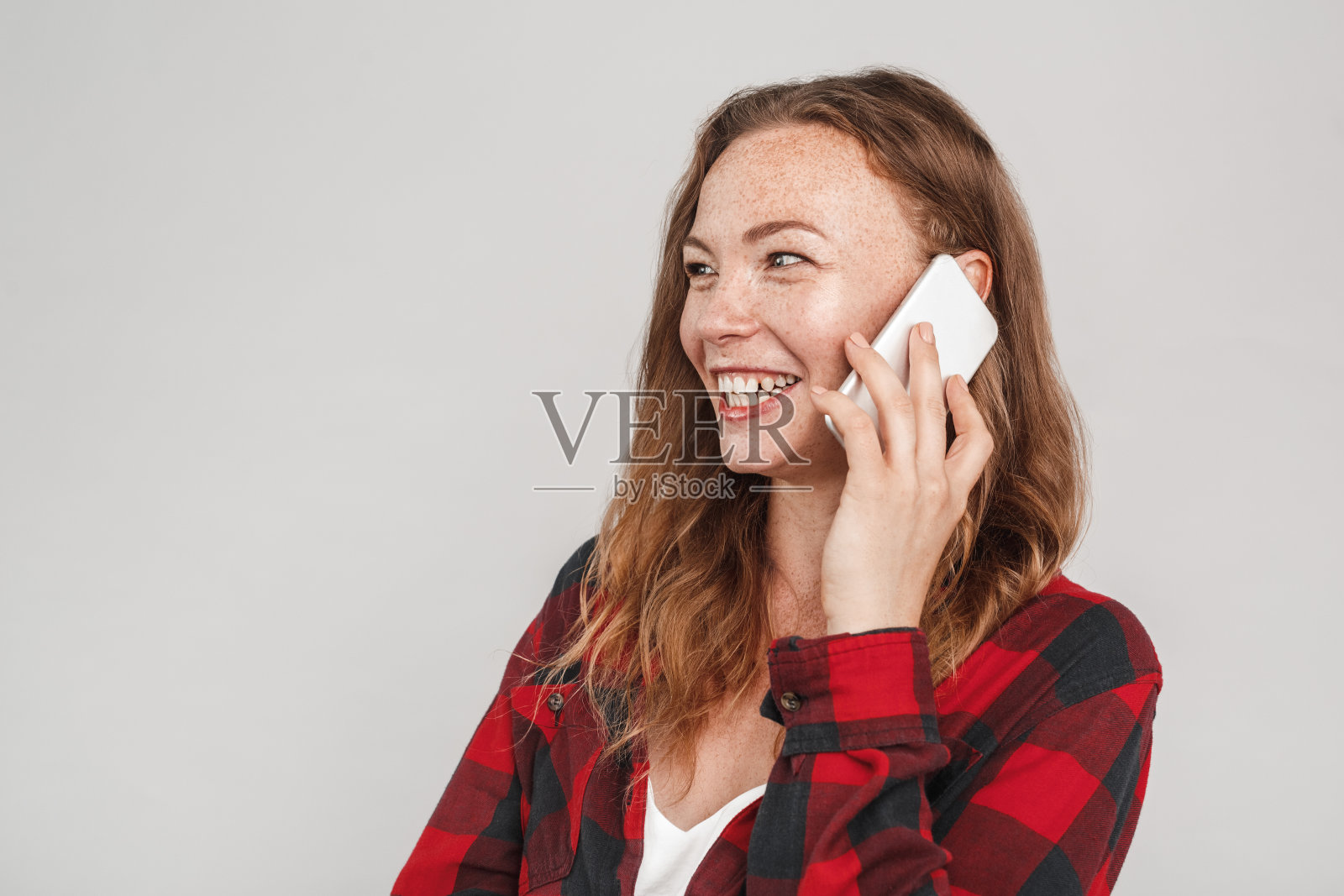 在灰色背景中，面带雀斑的年轻女子正在打电话，笑容满面照片摄影图片