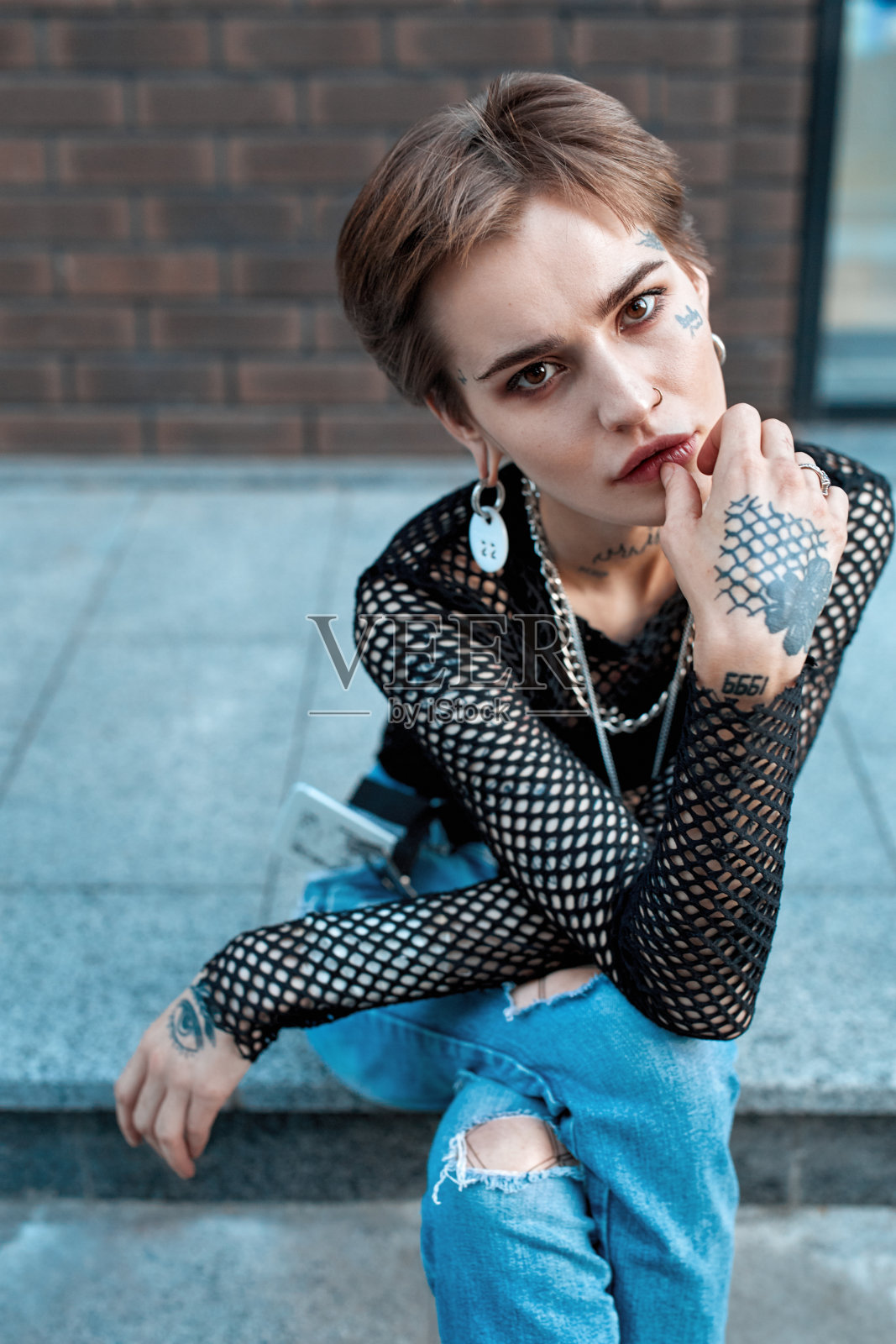 都市风尚：年轻时尚的女子坐在户外，喜悦地抚摸着嘴唇照片摄影图片