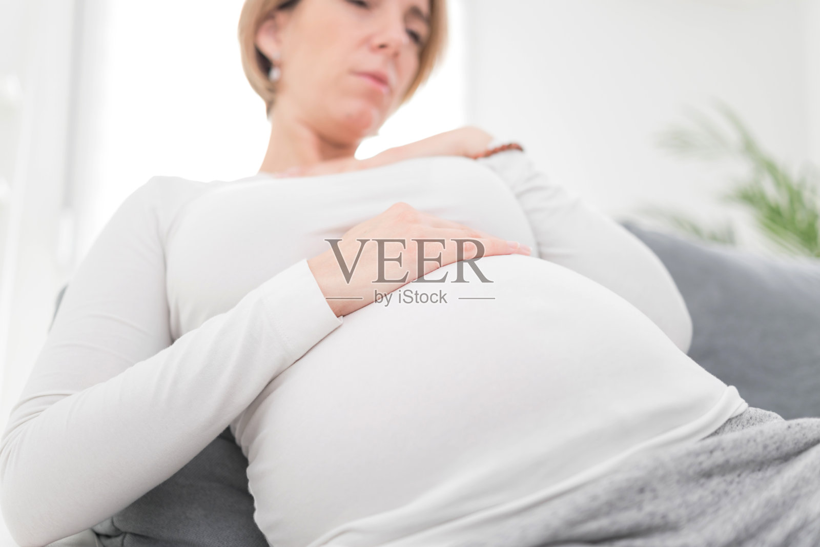 疲惫的孕妇在家中沙发上休息，有胃部不适。照片摄影图片