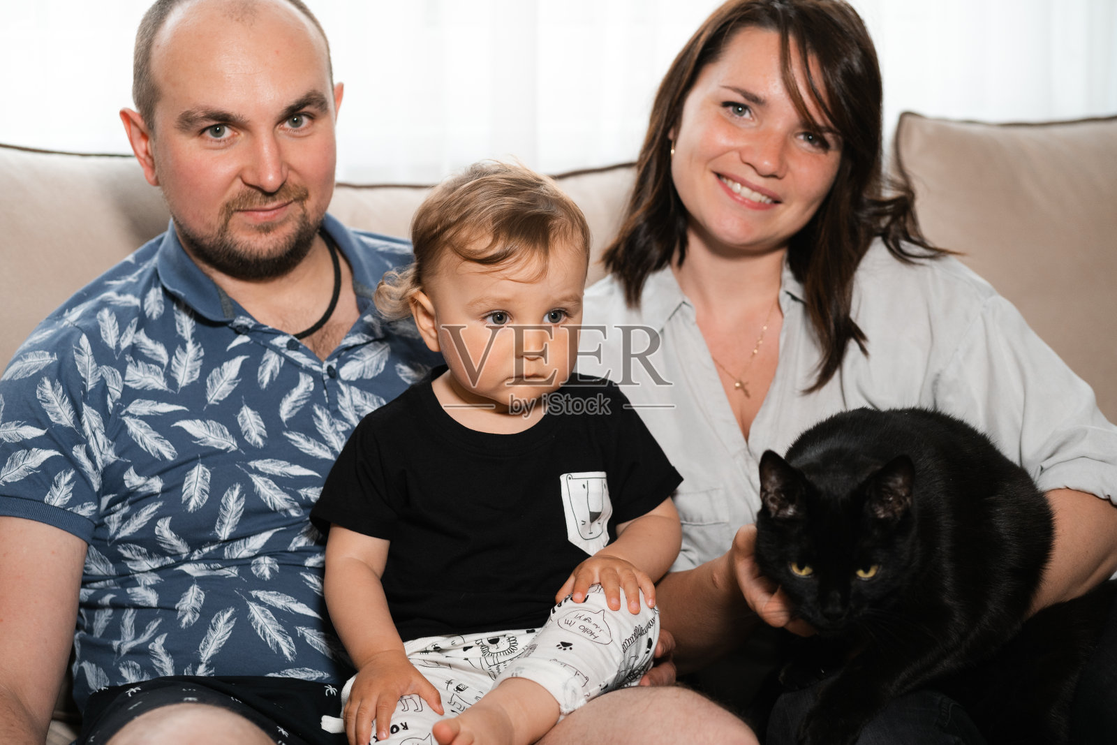 家庭:妈妈和爸爸在室内和小宝宝玩——父母穿着蓝色和灰色的家装，儿子穿着黑色和白色的家装——快乐的微笑的人照片摄影图片
