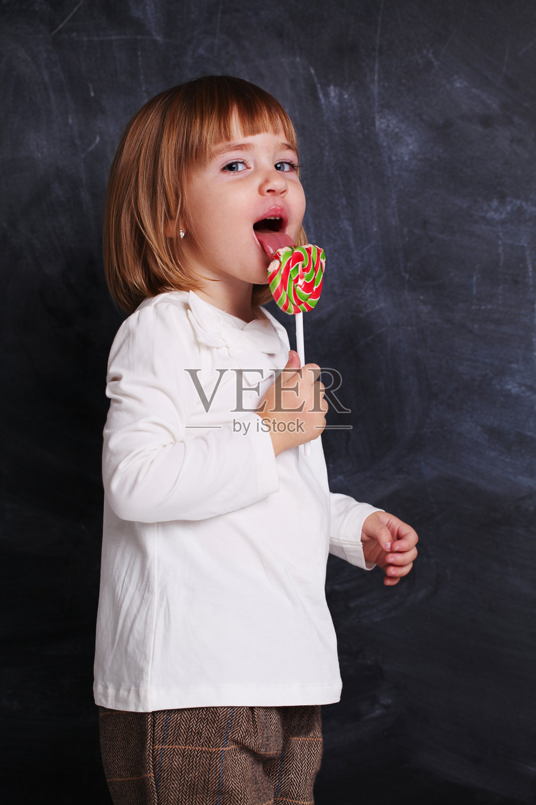 小女孩拿着一个五颜六色的棒棒糖。小孩子吃着棒棒糖。幸福的糖果女孩。享受。照片摄影图片