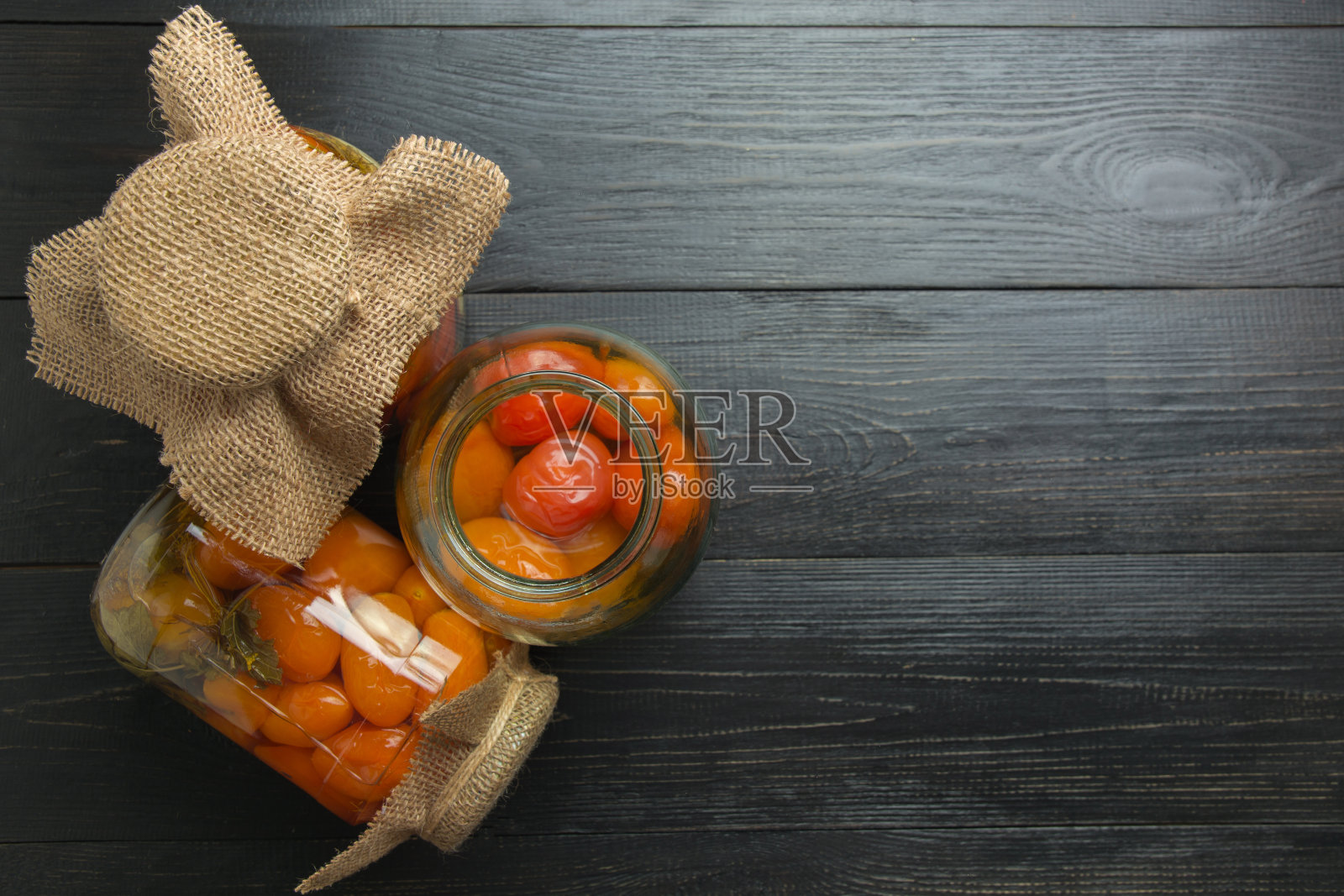 番茄罐头装在玻璃罐中，放在深色木板上。空间的文本。从以上观点。照片摄影图片