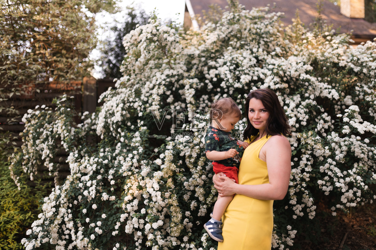 年轻母亲在公园里和宝宝玩耍，背景是鲜花盛开的树照片摄影图片