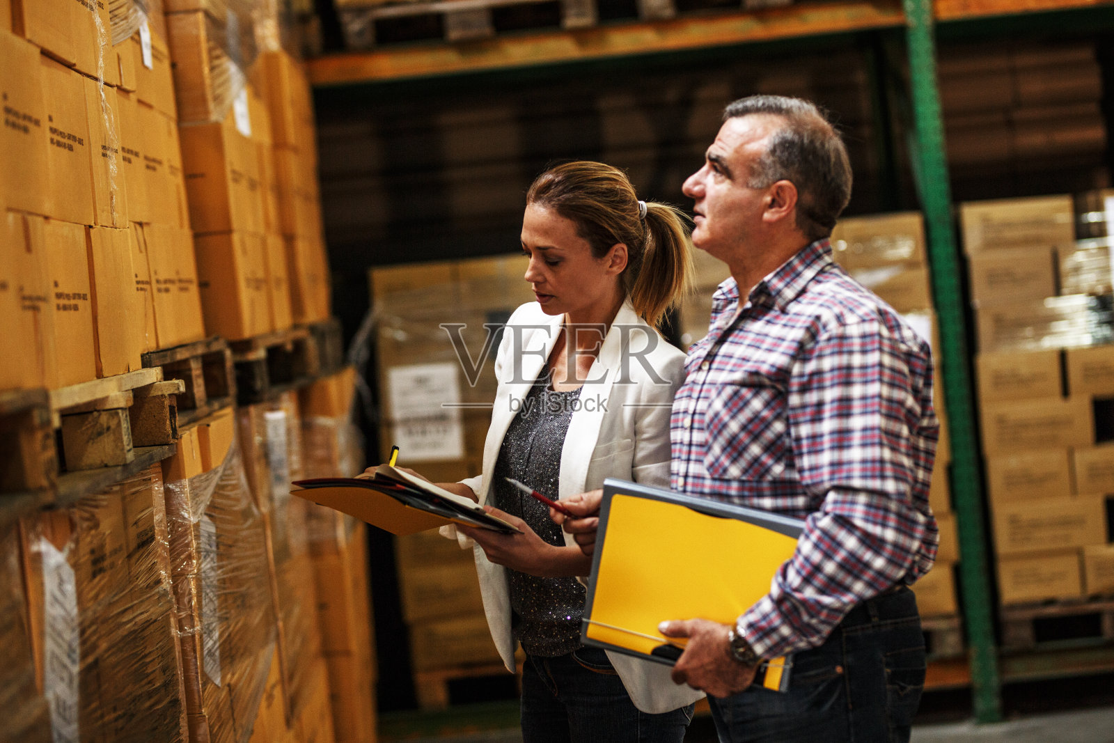 女经理和仓库工人检查仓库货架上的清单和存货。照片摄影图片