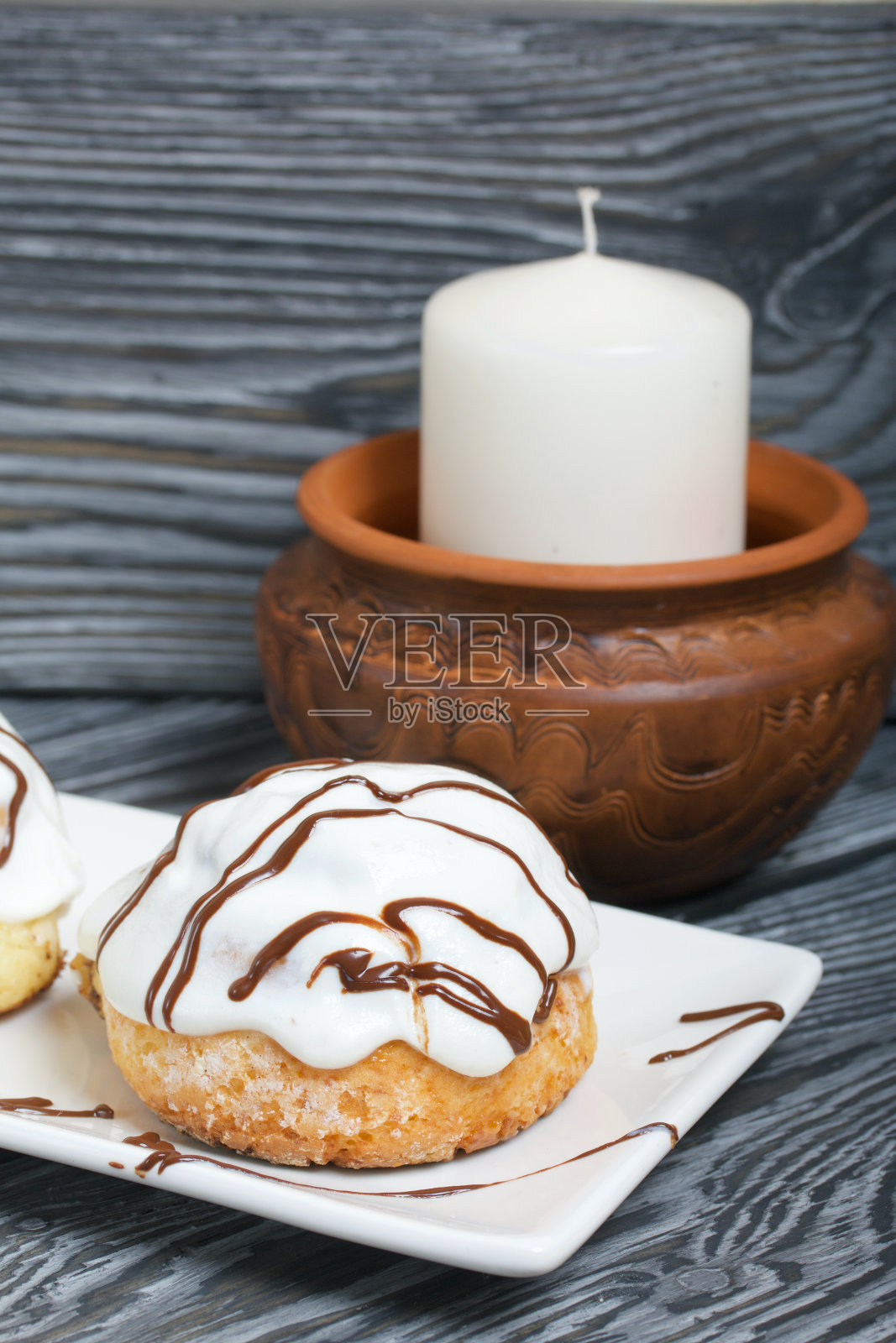 白釉肉桂粉，用巧克力装饰。躺在盘子上。旁边是一个粘土烛台上的白色蜡烛。以刷过的松木板为背景。照片摄影图片