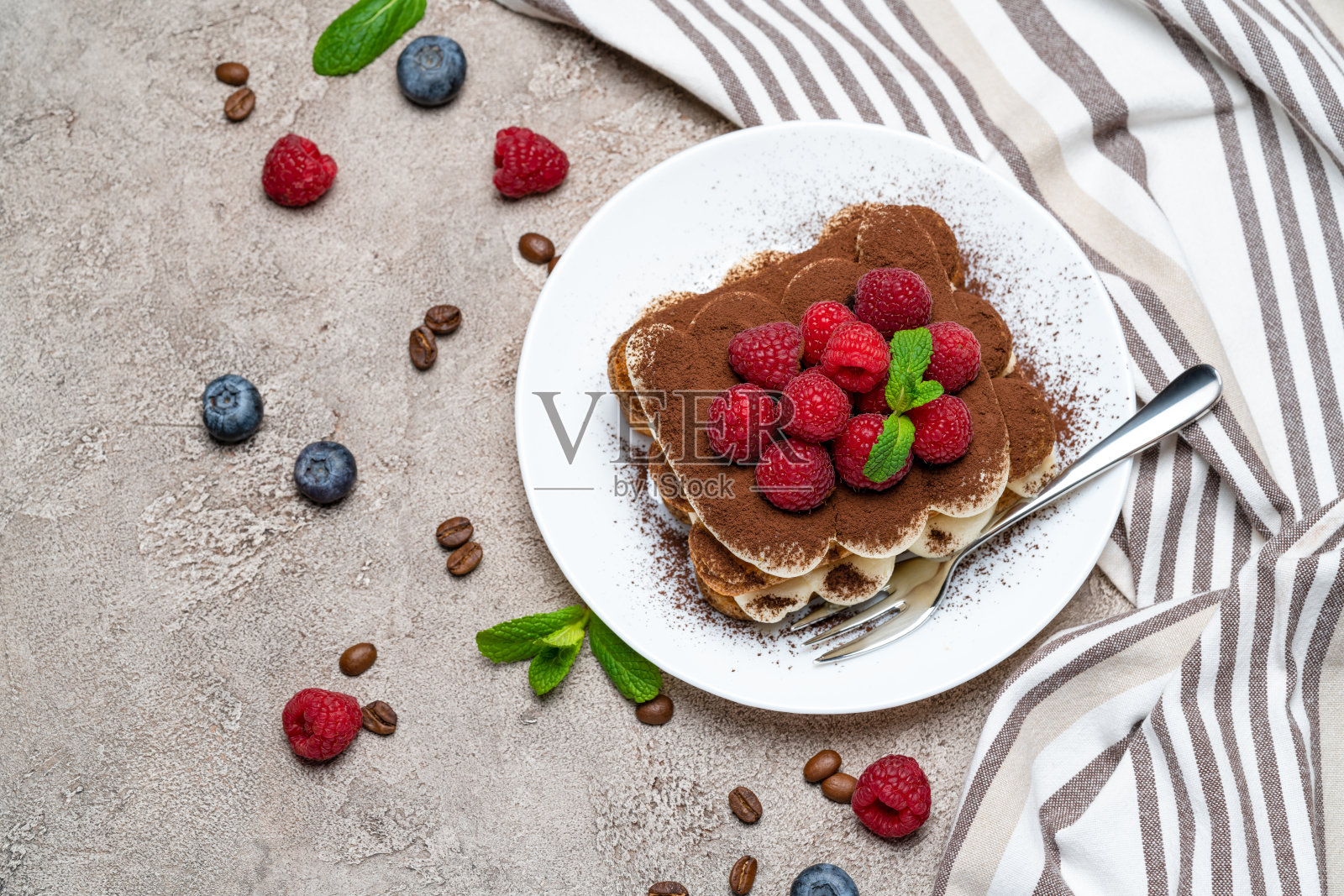 经典的提拉米苏甜点，在灰色的混凝土背景上点缀着覆盆子和蓝莓照片摄影图片