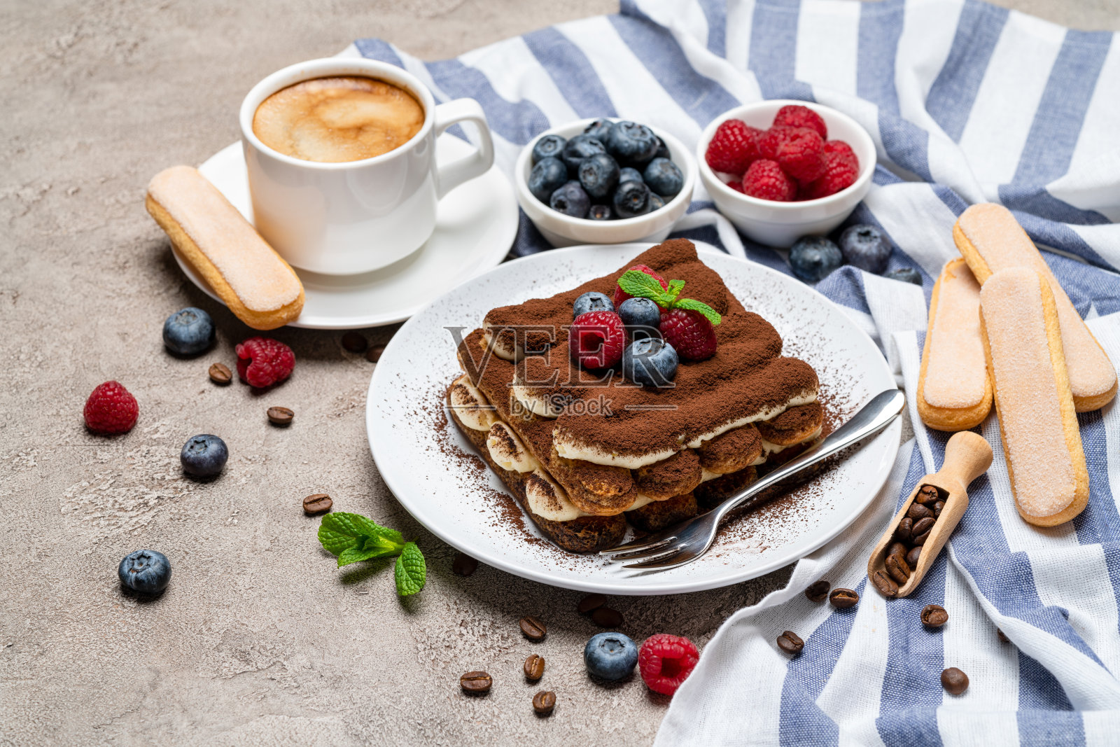 一份经典的提拉米苏甜点，配上覆盆子、蓝莓和一杯在灰色混凝土背景上的咖啡照片摄影图片