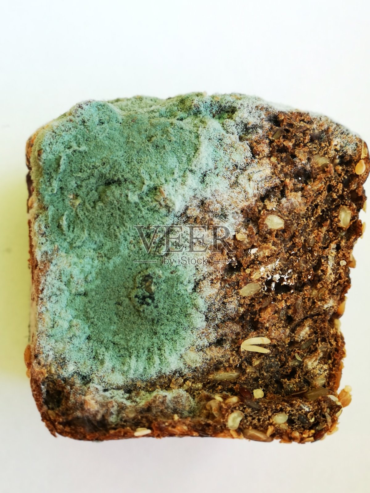 白色背景上有绿色霉菌的部分谷物面包照片摄影图片