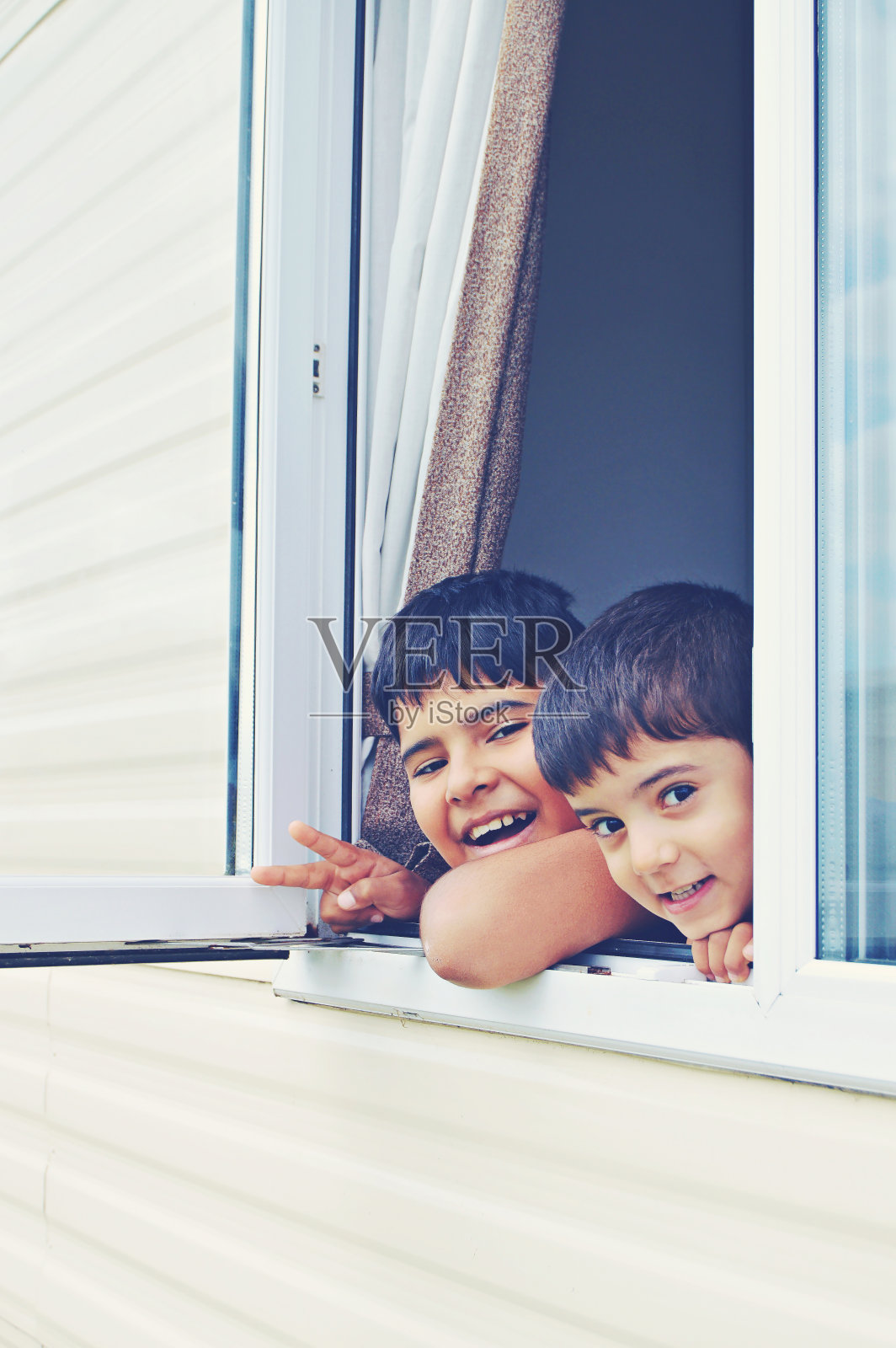 两个男孩的垂直照片，透过一扇开着的窗户和快乐的面部表情窥视照片摄影图片