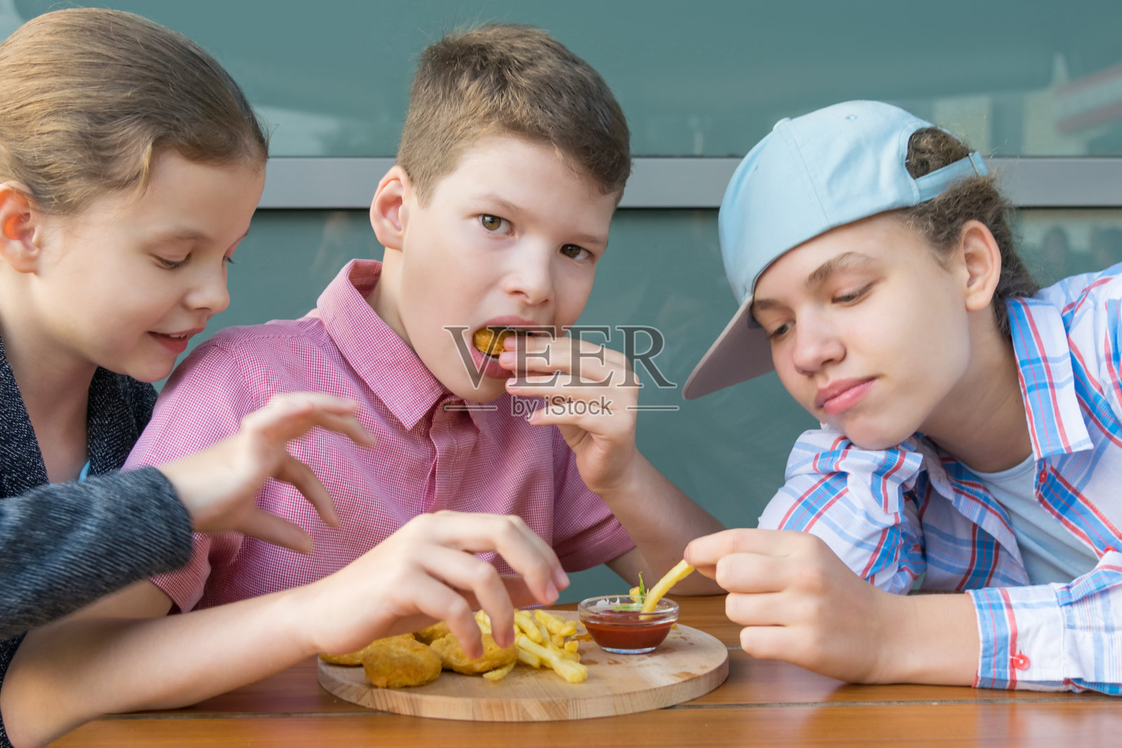 两个女孩和一个男孩在快餐店的桌旁吃带酱汁的虾照片摄影图片