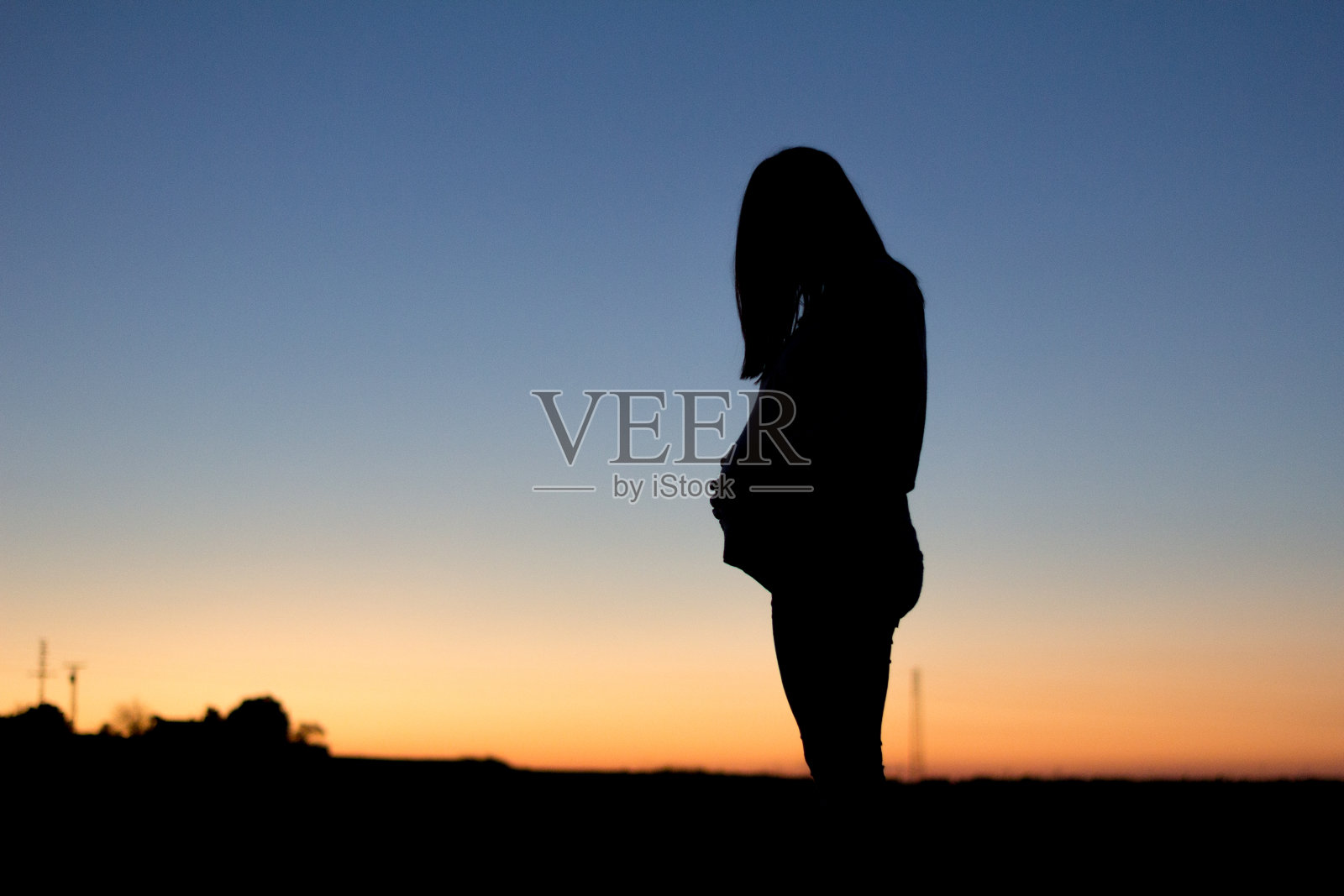 一位孕妇摸着自己的肚子，在色彩斑斓的阳光下显现出轮廓照片摄影图片