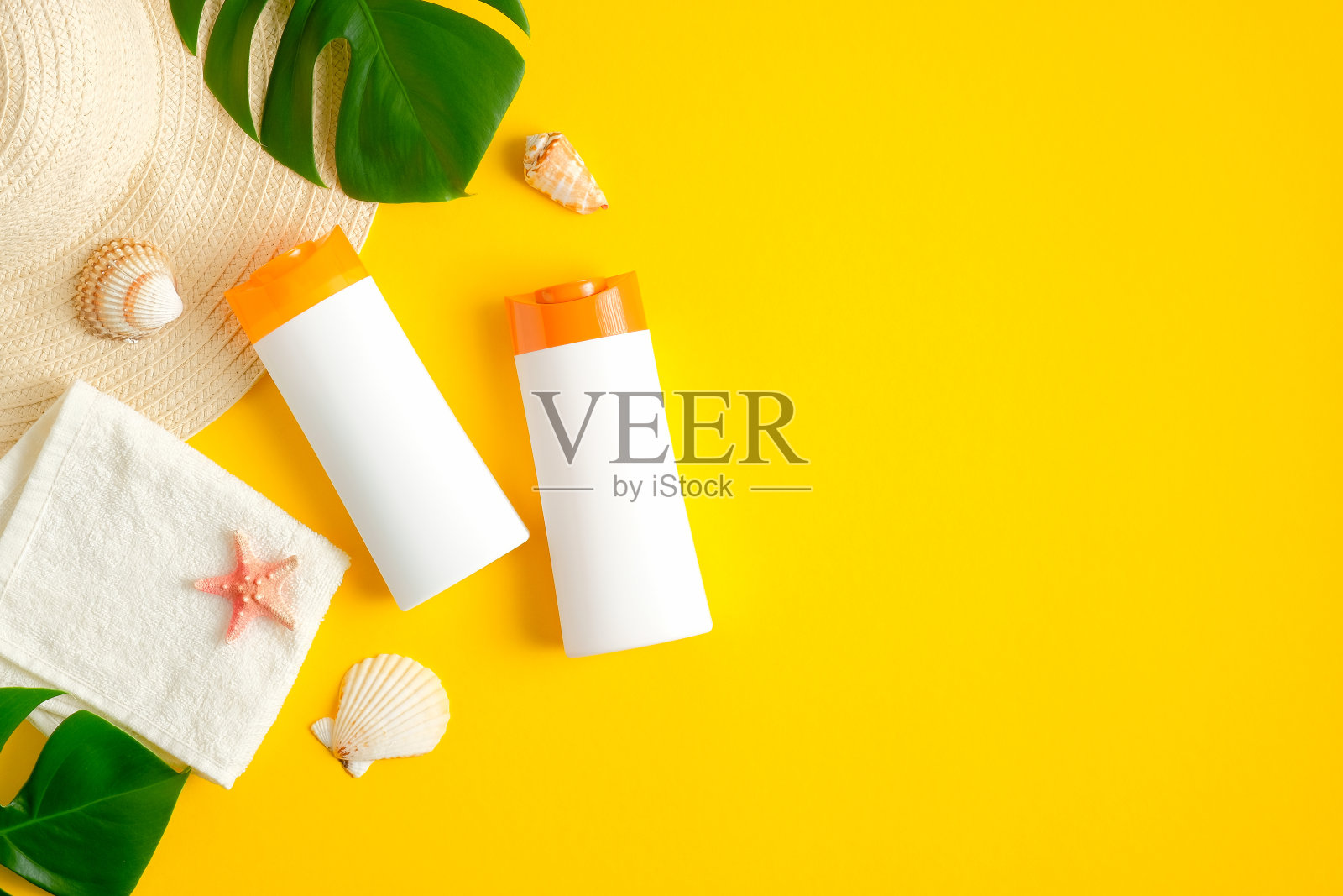 防晒霜瓶子，热带树叶，毛巾，贝壳在黄色的背景。平躺，俯视图。防晒、晒黑化妆品、夏日护肤理念照片摄影图片