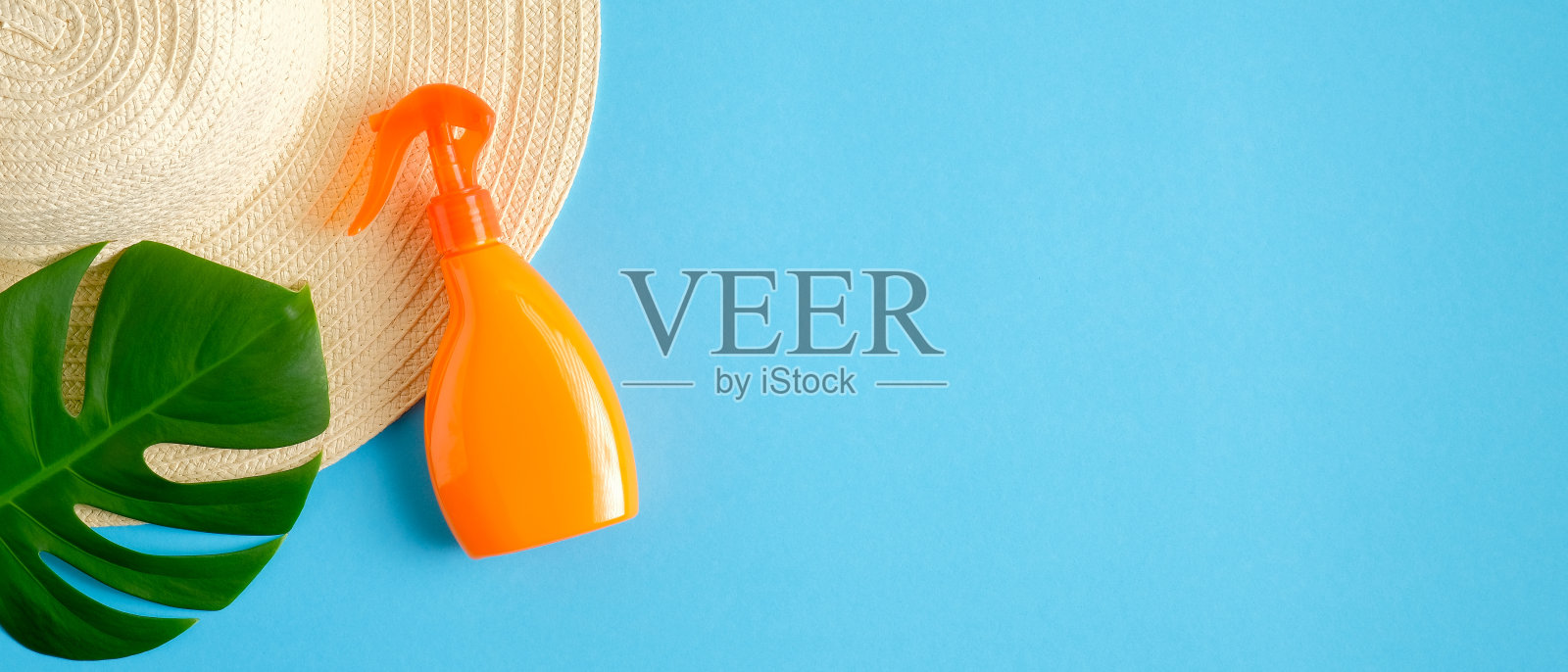防晒喷雾瓶，女性沙滩帽和热带绿叶孤立在蓝色背景。防晒和晒黑化妆品概念。平躺，俯视图照片摄影图片