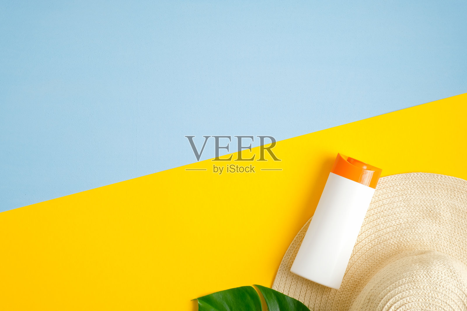 防晒霜瓶，绿色热带树叶，女性沙滩帽隔离在蓝色和黄色的背景。防晒、晒黑化妆品、护肤理念。平躺，俯视图照片摄影图片