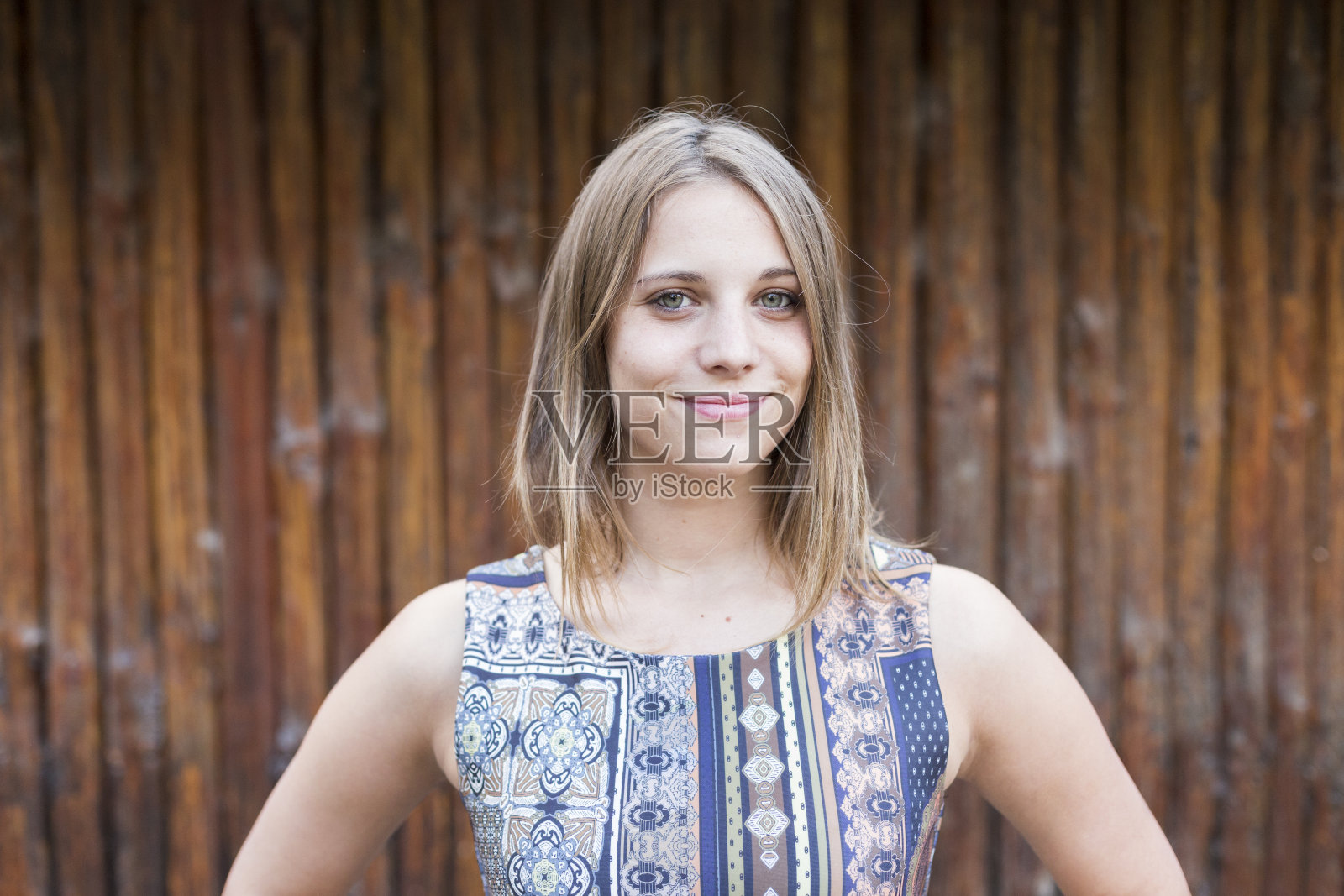 户外肖像的一个美丽的年轻女子看着相机和微笑。木头的背景照片摄影图片