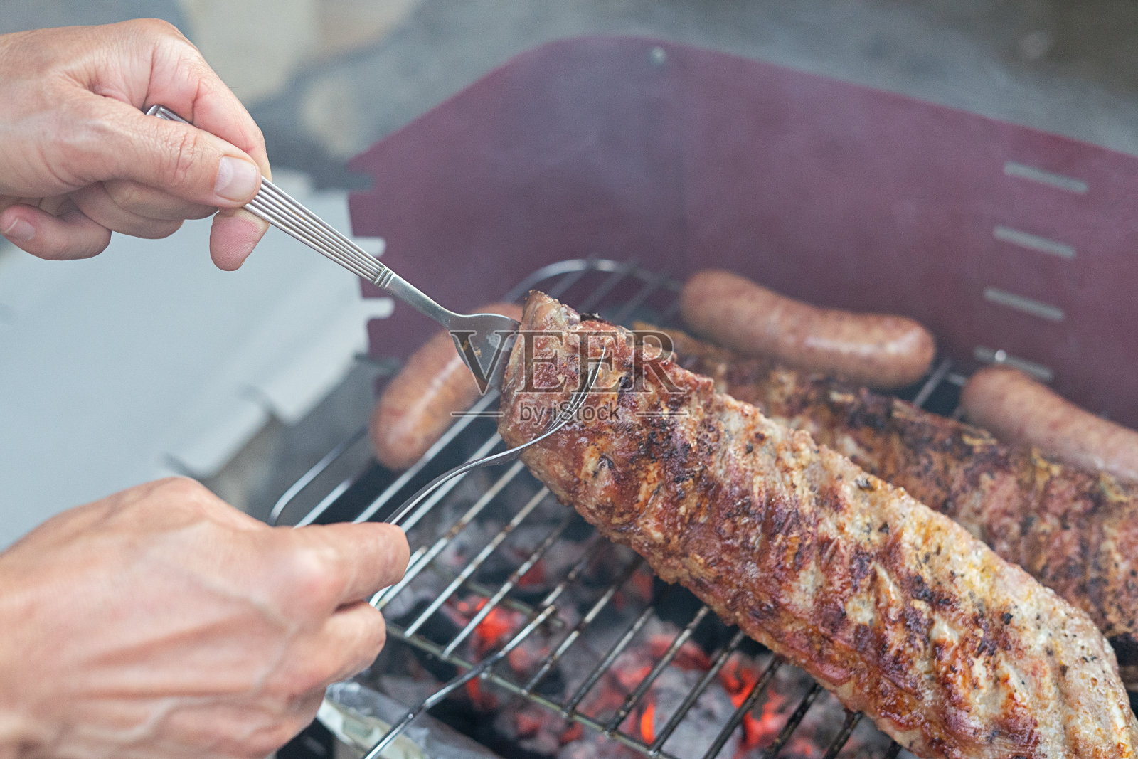 用手翻烤炭火烤架上的猪排。美食概念。留白照片摄影图片