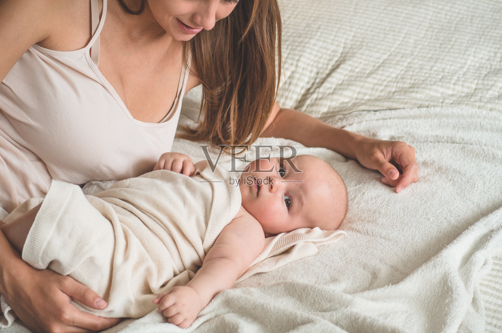 新生儿和母亲在床上的家庭肖像。妈妈抱着并亲吻她的孩子照片摄影图片