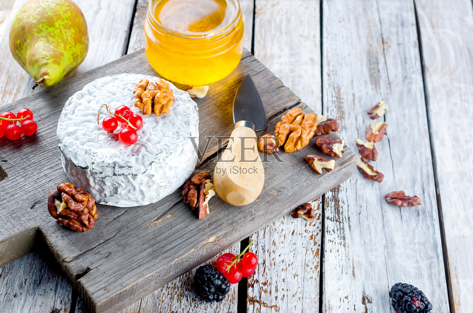 一块木板上放着各种美味的奶酪，白色的旧木桌上放着坚果、蜂蜜、浆果、橄榄等小吃。食品配料的背景。有选择性的重点。“n照片摄影图片