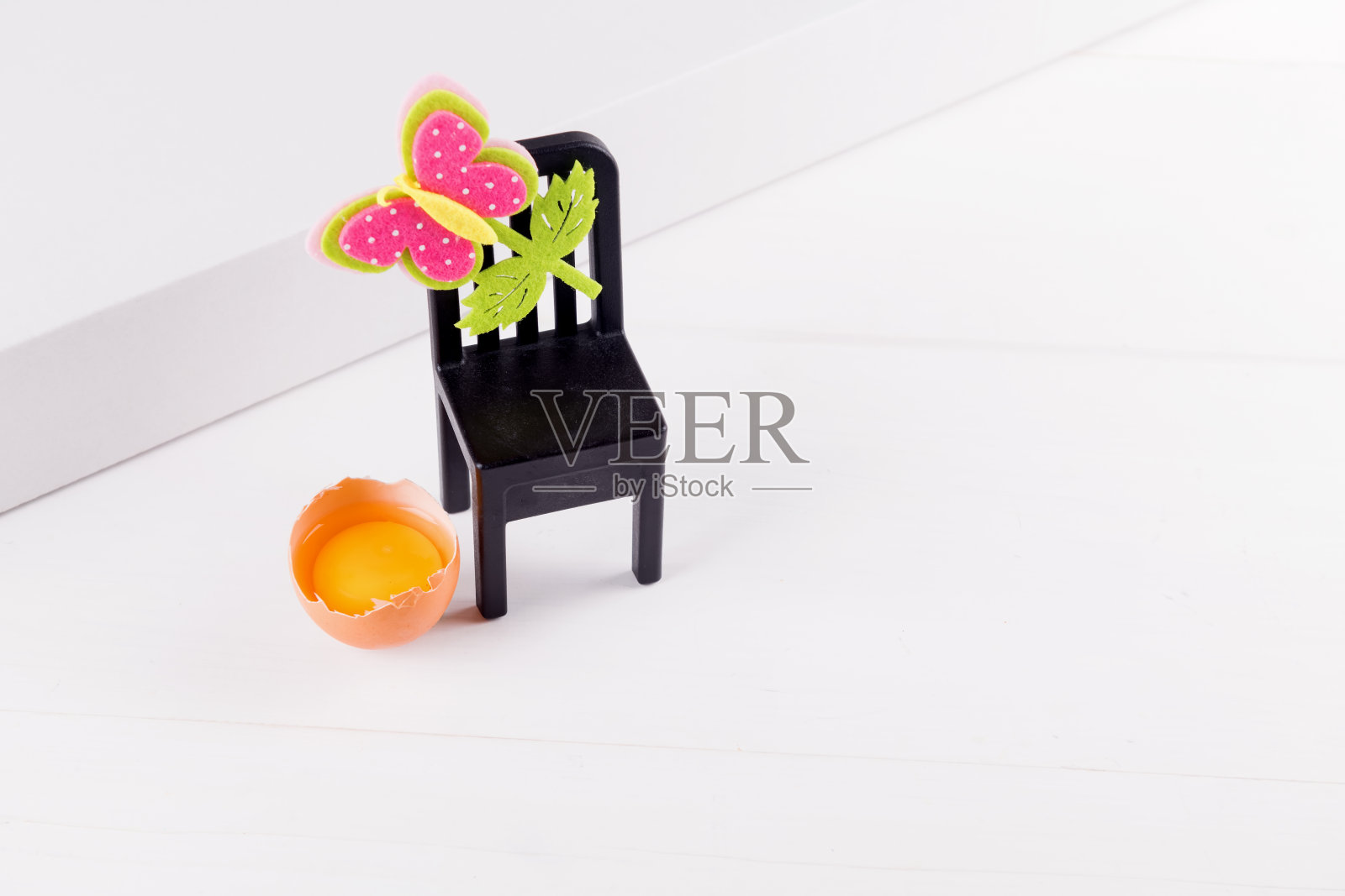 白色的桌子上放着半个生鸡蛋和蛋黄，黑色的椅子上装饰着复活节花。最小复活节概念构思，选择性重点照片摄影图片