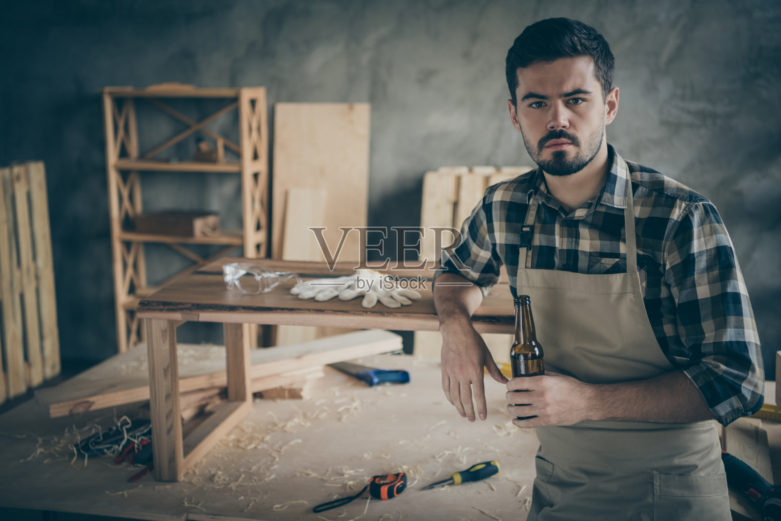 认真成功的工人，硬木企业家做了他的平板桌子修复工作，休息，放松，在家里的房子的车库中持有玻璃瓶啤酒照片摄影图片