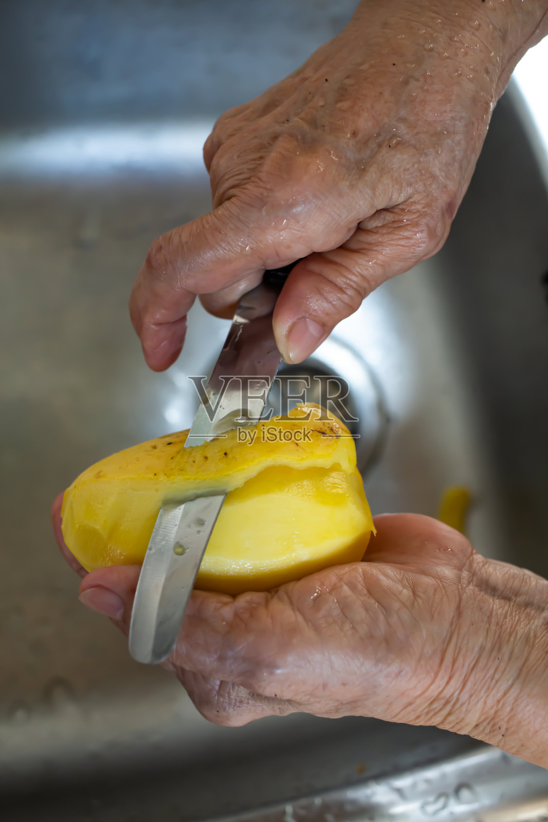 年长女性用刀在水槽中削芒果皮特写，泰国传统水果照片摄影图片