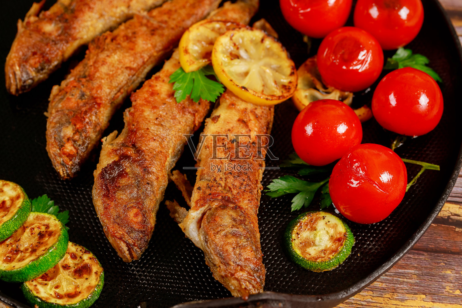 美味的炸鱼配蔬菜放在黑煎锅里。关闭了。照片摄影图片