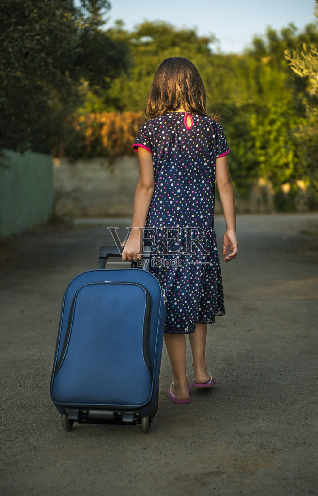 后视图的一个小女孩走在道路上拉手提箱照片摄影图片