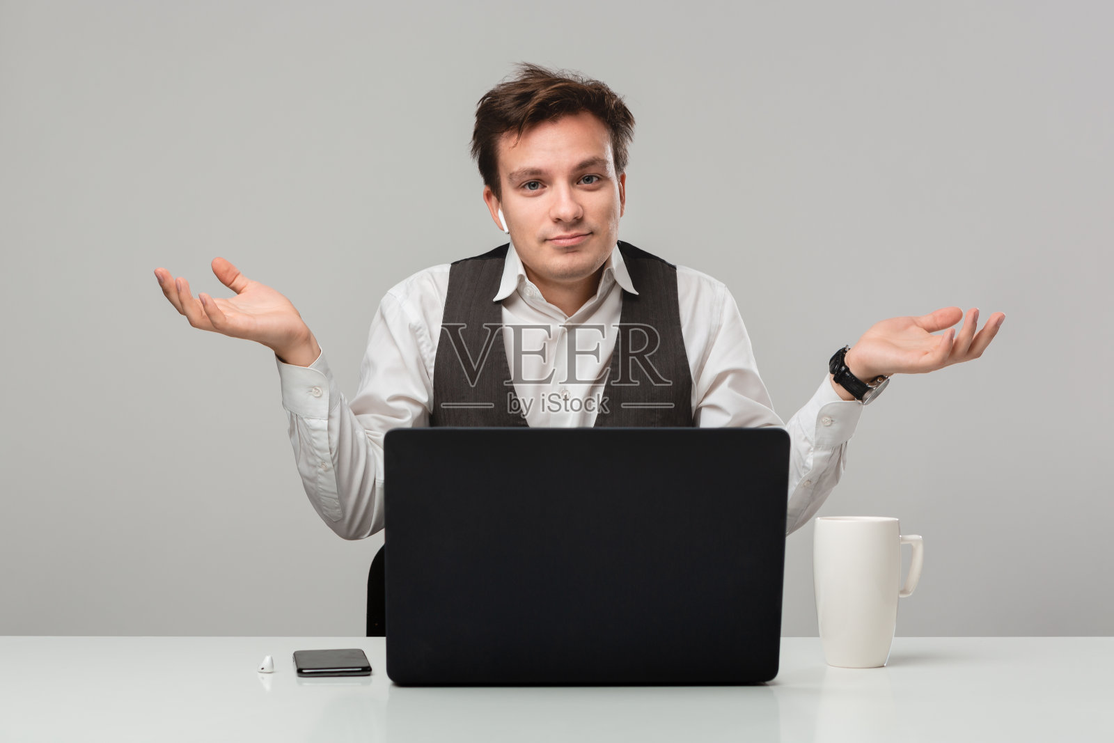 尴尬的男人耸耸肩，看着镜头，坐在白色桌子旁，无言以对照片摄影图片