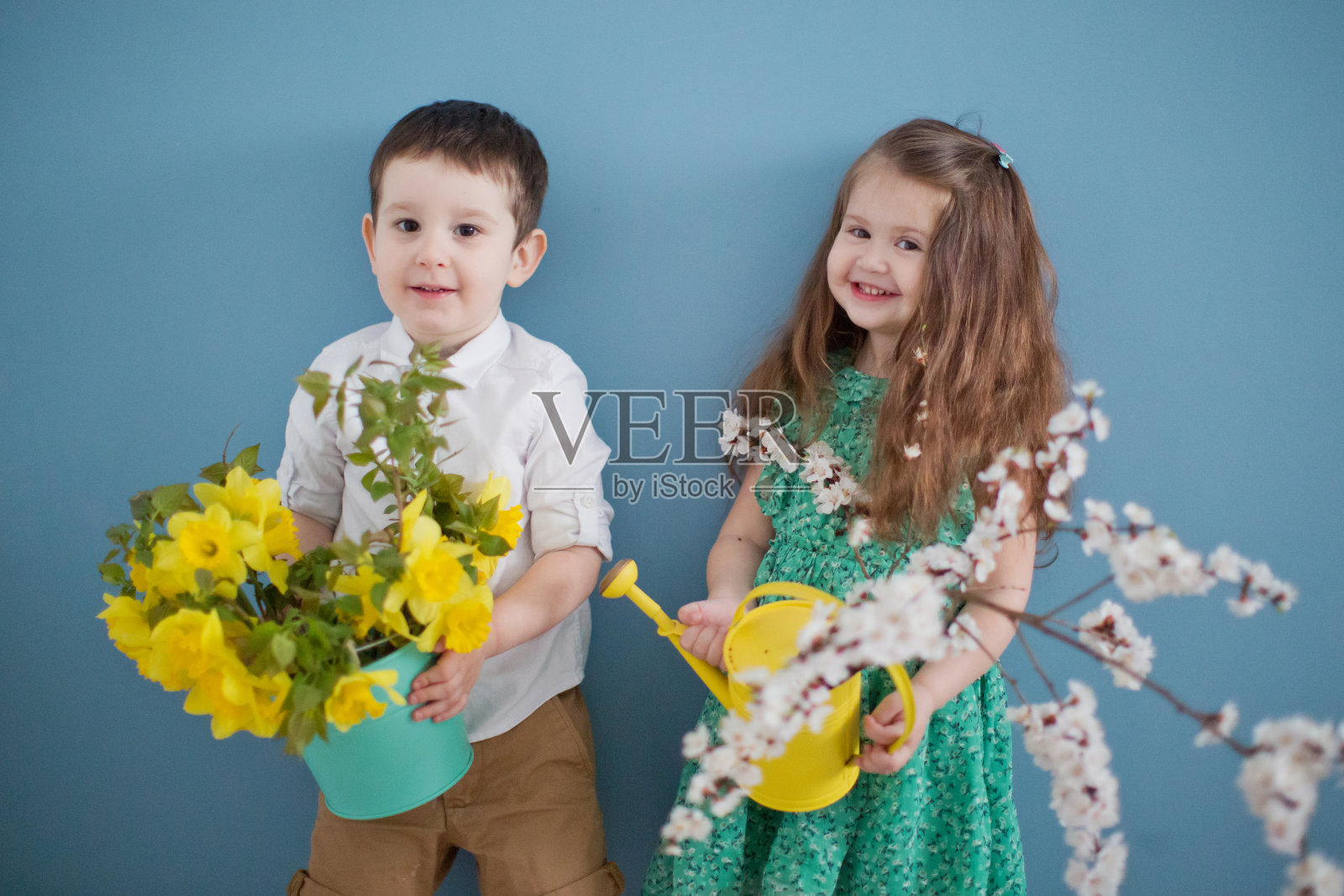 蹒跚学步的男孩和女孩拿着水仙花和杏花的树枝。照片摄影图片