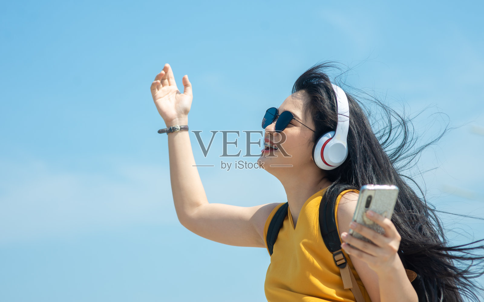 在海滩上戴着耳机，背着背包的快乐亚洲女人照片摄影图片