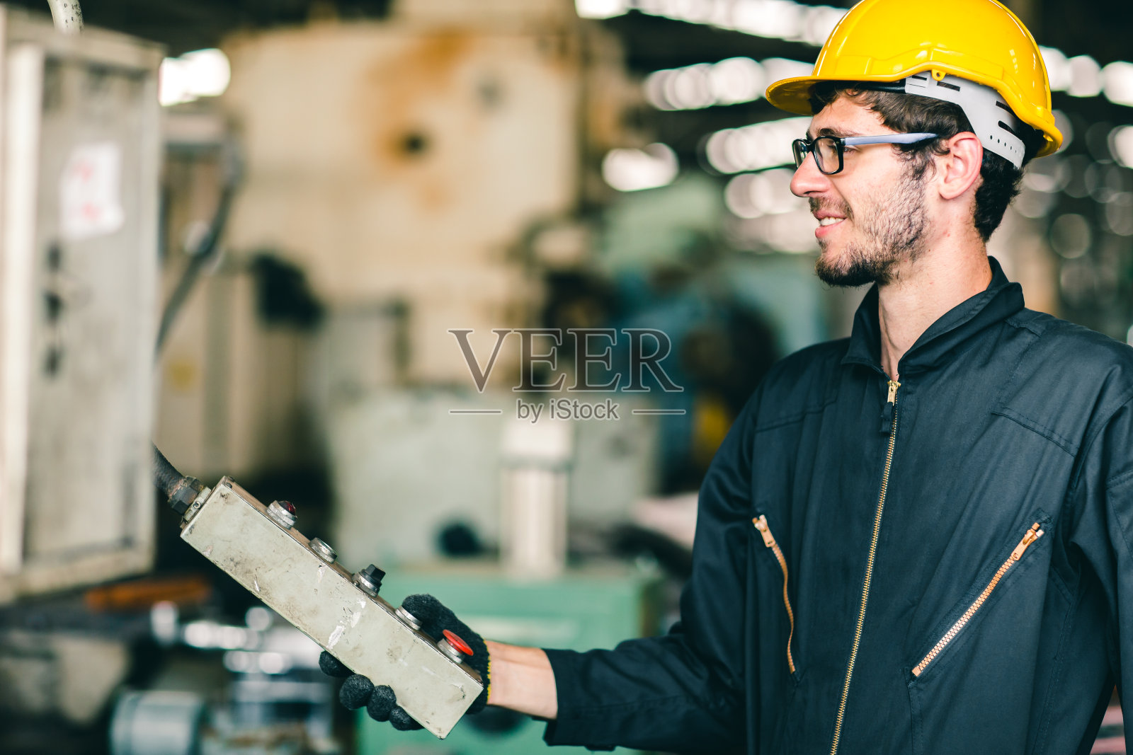 劳动工人在工业工厂里穿着安全服和头盔，快乐地笑着，享受着操作重型机器的工作。照片摄影图片