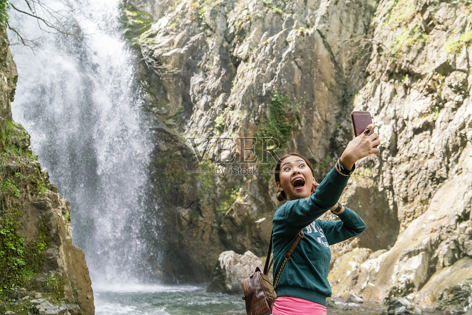亚洲女性独自旅行，在瀑布边用手机拍照照片摄影图片